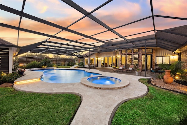 pool at dusk with a yard, an in ground hot tub, glass enclosure, and a patio