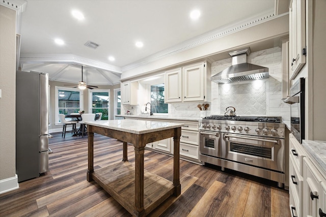 kitchen featuring stainless steel appliances, ceiling fan, dark hardwood / wood-style floors, decorative backsplash, and wall chimney range hood