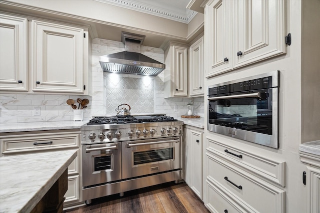 kitchen with stainless steel appliances, ornamental molding, light stone counters, decorative backsplash, and wall chimney range hood