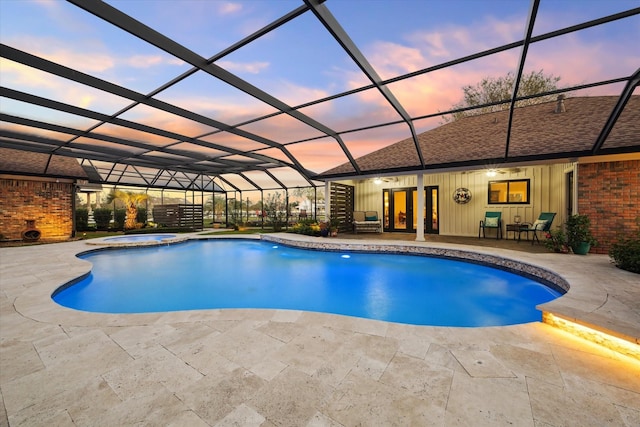 pool at dusk featuring a lanai, a patio area, and an in ground hot tub