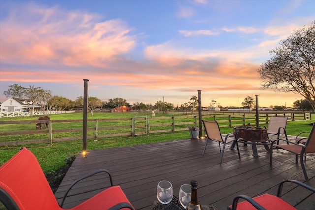 deck at dusk with an outdoor fire pit, a rural view, and a lawn