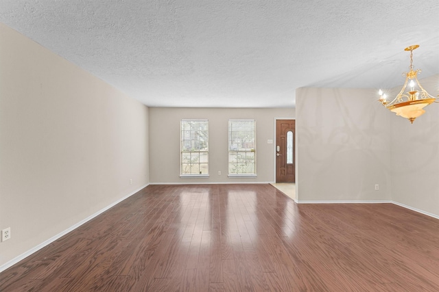 empty room featuring dark hardwood / wood-style flooring, an inviting chandelier, and a textured ceiling