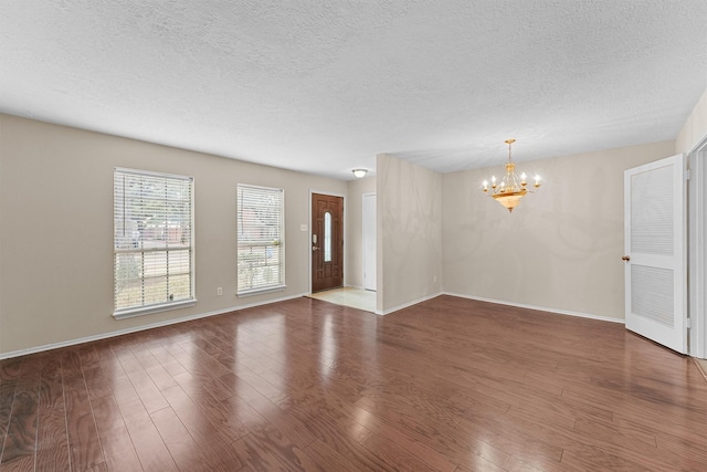 spare room with a textured ceiling, hardwood / wood-style flooring, and a notable chandelier