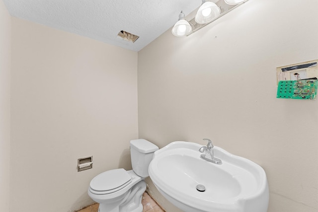 bathroom with toilet, tile patterned flooring, a textured ceiling, and sink