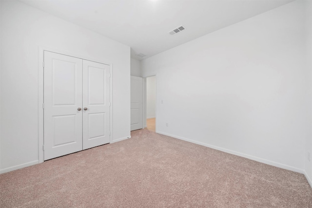 unfurnished bedroom with light colored carpet and a closet