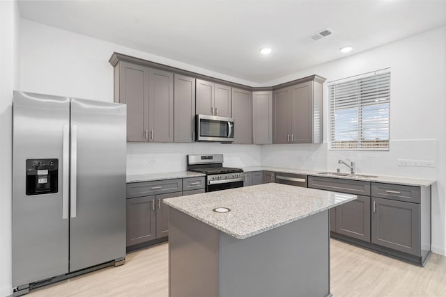 kitchen featuring appliances with stainless steel finishes, gray cabinetry, light stone countertops, a kitchen island, and sink