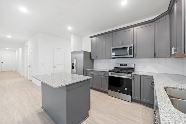 kitchen with appliances with stainless steel finishes, gray cabinetry, a kitchen island, light hardwood / wood-style flooring, and light stone counters