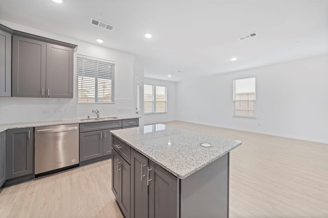 kitchen featuring light stone countertops, a kitchen island, sink, light wood-type flooring, and stainless steel dishwasher