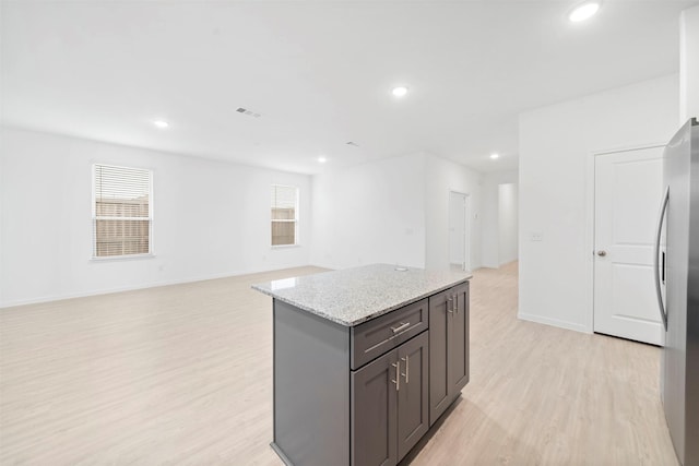 kitchen with light wood-type flooring, stainless steel refrigerator, light stone counters, and a kitchen island