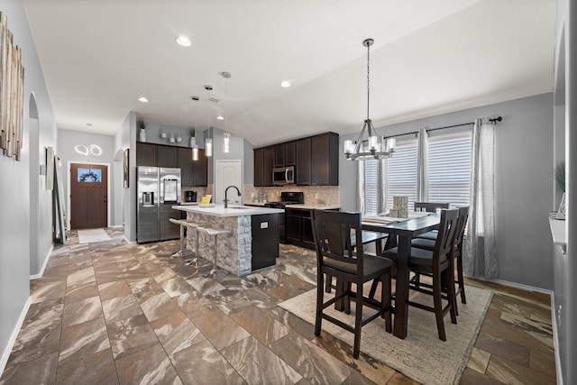 kitchen with dark brown cabinets, appliances with stainless steel finishes, sink, a kitchen island with sink, and decorative backsplash