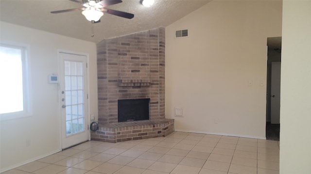 unfurnished living room featuring light tile patterned floors, ceiling fan, a brick fireplace, lofted ceiling, and a textured ceiling