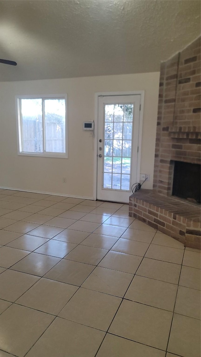 unfurnished living room with ceiling fan, a textured ceiling, tile patterned floors, and a fireplace