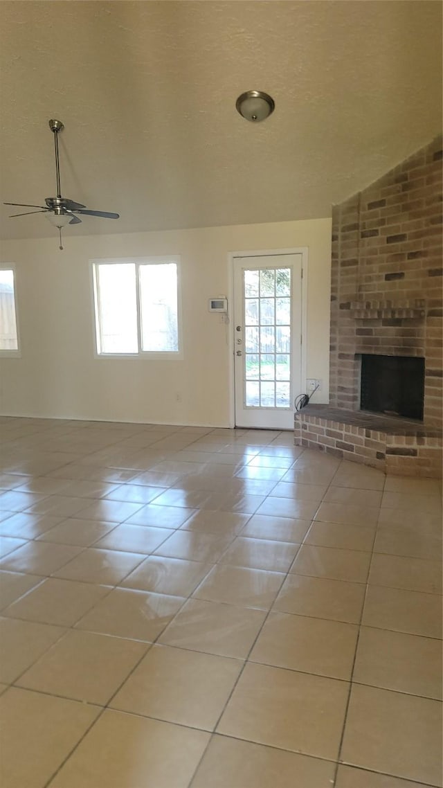 unfurnished living room with ceiling fan, light tile patterned floors, lofted ceiling, and a brick fireplace