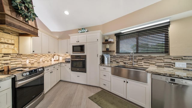 kitchen with sink, custom exhaust hood, appliances with stainless steel finishes, light stone countertops, and white cabinets