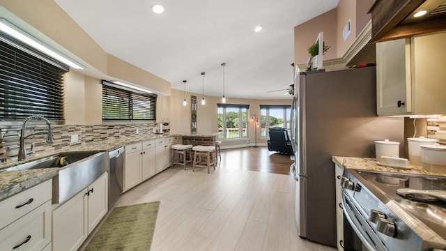 kitchen with tasteful backsplash, white cabinetry, light stone counters, hanging light fixtures, and appliances with stainless steel finishes