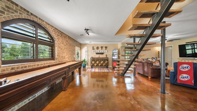 playroom with ceiling fan, concrete floors, a textured ceiling, and brick wall