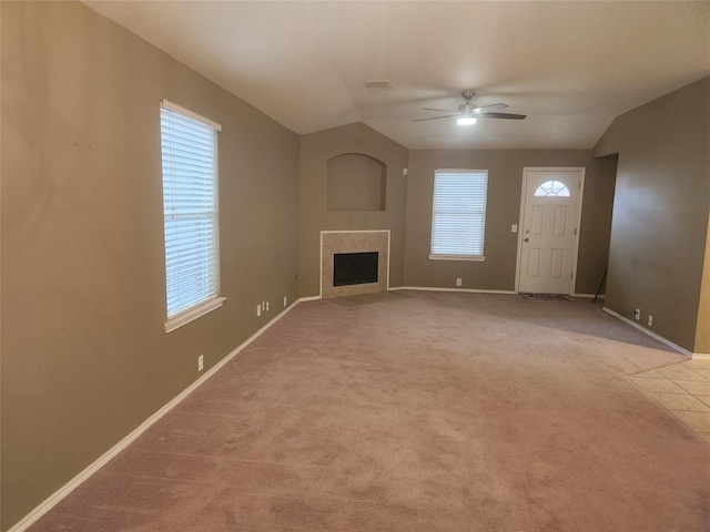 unfurnished living room featuring a tile fireplace, lofted ceiling, a wealth of natural light, and light colored carpet