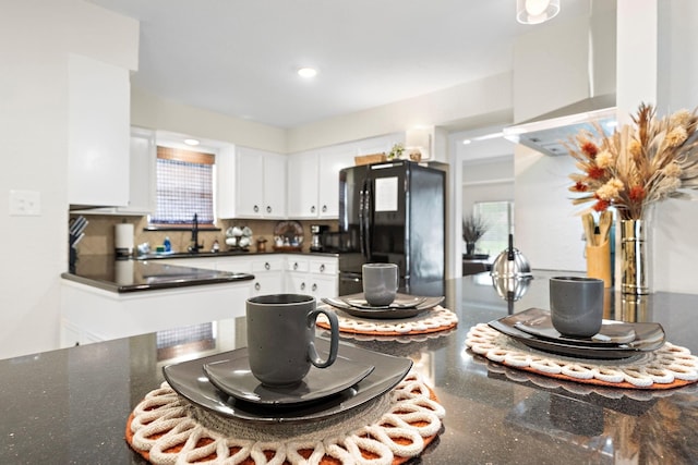 kitchen with sink, white cabinets, black fridge, backsplash, and wall chimney range hood