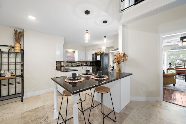 kitchen featuring kitchen peninsula, black fridge, a breakfast bar area, white cabinets, and ceiling fan