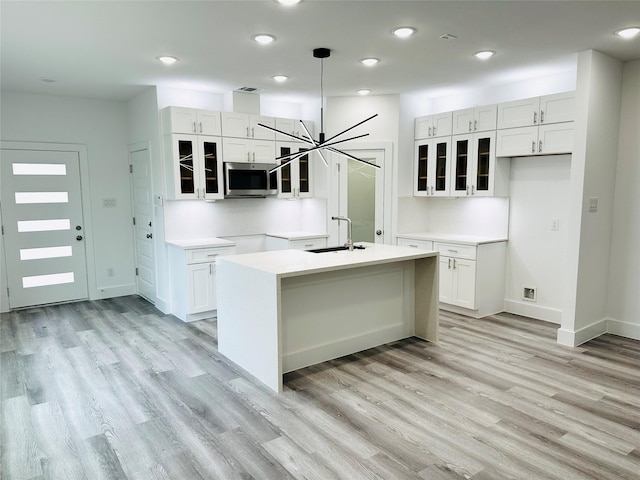 kitchen featuring decorative light fixtures, white cabinetry, sink, a kitchen island with sink, and a notable chandelier