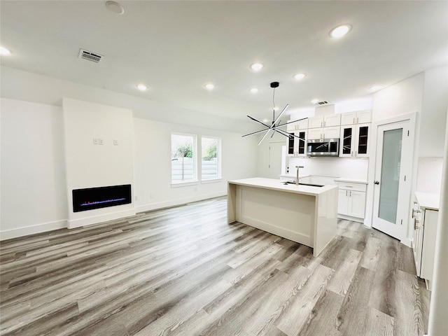 kitchen with pendant lighting, white cabinetry, an inviting chandelier, light hardwood / wood-style floors, and a center island with sink