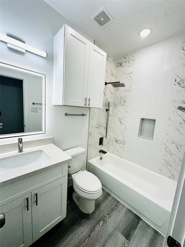 full bathroom with hardwood / wood-style floors, tiled shower / bath combo, vanity, and toilet