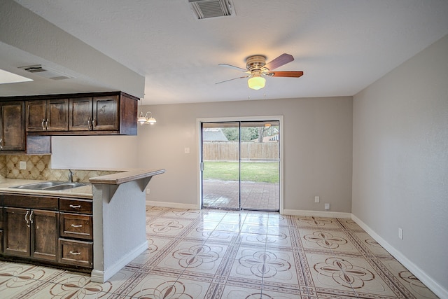 kitchen with ceiling fan with notable chandelier, decorative backsplash, sink, kitchen peninsula, and dark brown cabinets