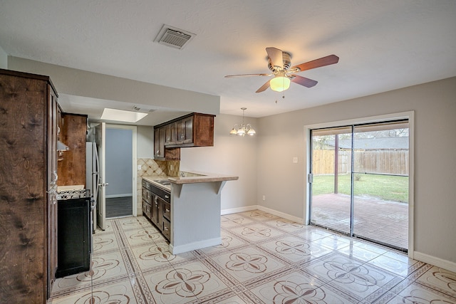 kitchen featuring decorative backsplash, gas stove, stainless steel refrigerator, ceiling fan with notable chandelier, and dark brown cabinetry