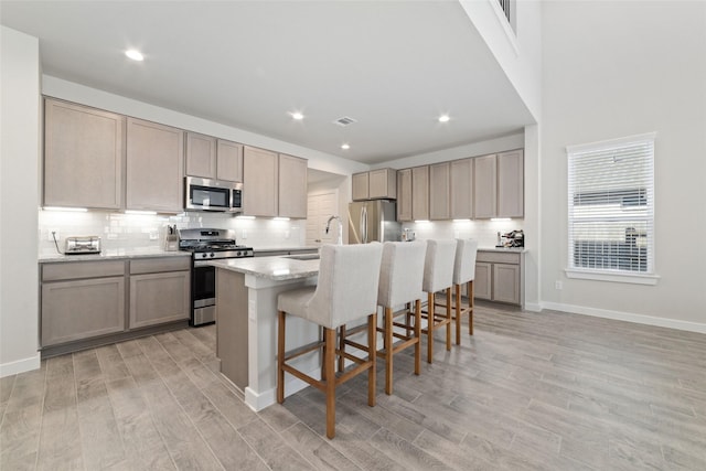 kitchen featuring a kitchen breakfast bar, appliances with stainless steel finishes, an island with sink, light wood-type flooring, and sink