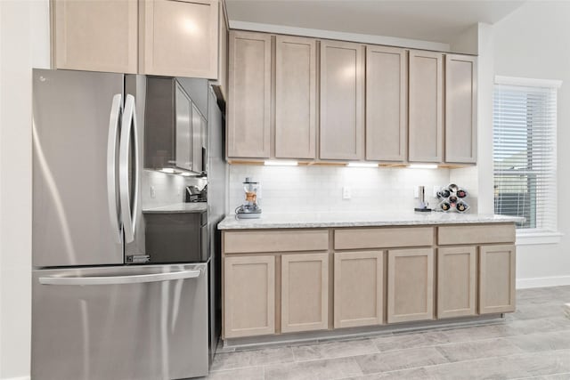 kitchen with light stone countertops, light brown cabinets, backsplash, and stainless steel fridge