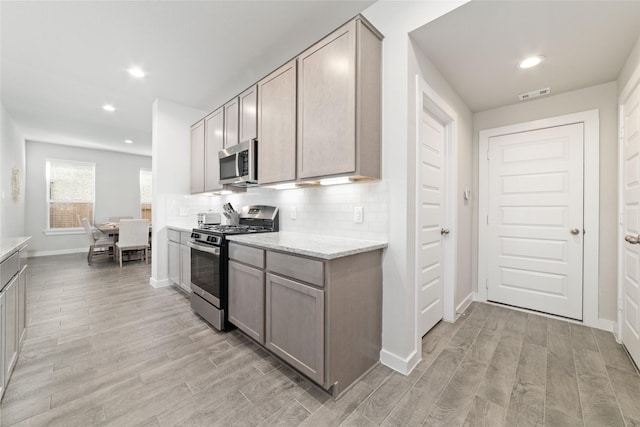 kitchen featuring light stone counters, stainless steel appliances, gray cabinets, and decorative backsplash