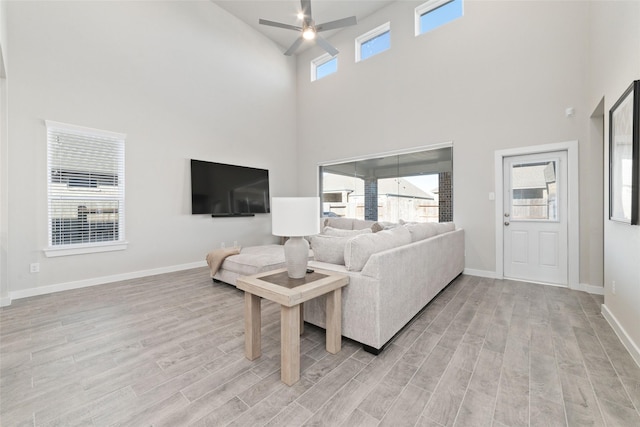 living room with ceiling fan, light wood-type flooring, a towering ceiling, and a wealth of natural light