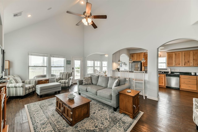 living room featuring a towering ceiling, ceiling fan, dark hardwood / wood-style flooring, and a wealth of natural light