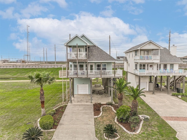 coastal home featuring covered porch, a balcony, a front lawn, and a garage