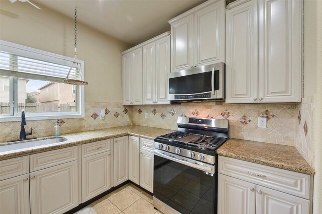 kitchen featuring stainless steel appliances, light tile patterned floors, sink, white cabinetry, and backsplash