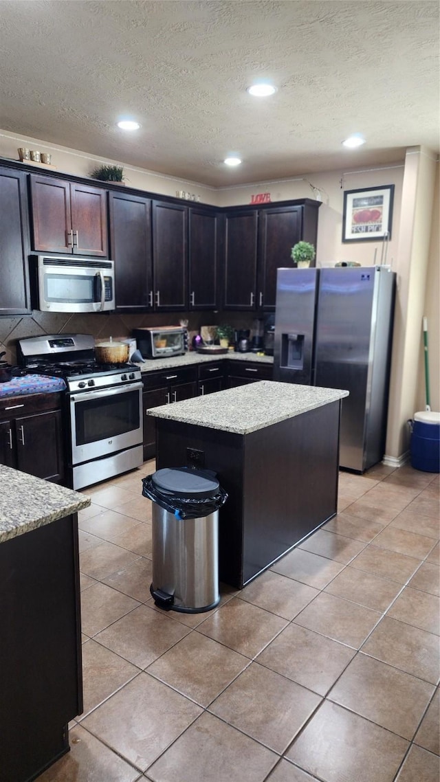 kitchen featuring appliances with stainless steel finishes, light stone countertops, a textured ceiling, and a kitchen island