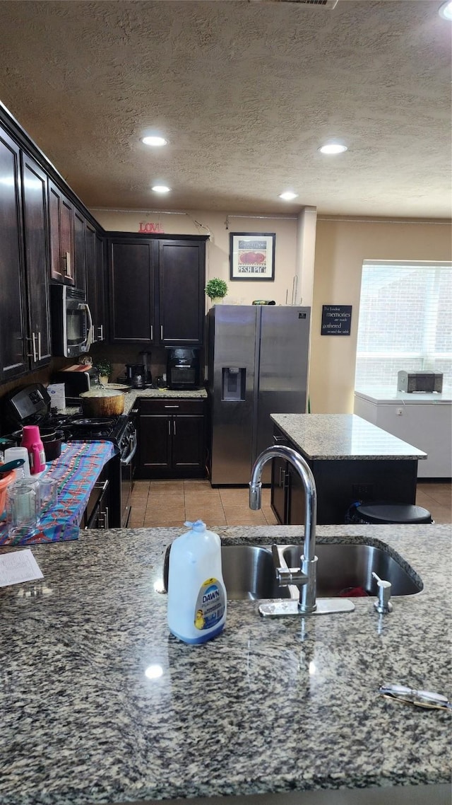 kitchen featuring stainless steel appliances, light stone countertops, a textured ceiling, dark brown cabinets, and sink