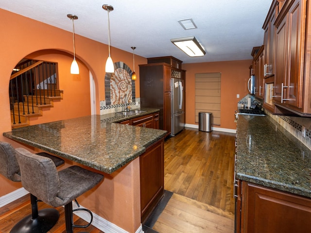 kitchen featuring dark hardwood / wood-style floors, pendant lighting, dark stone counters, and kitchen peninsula