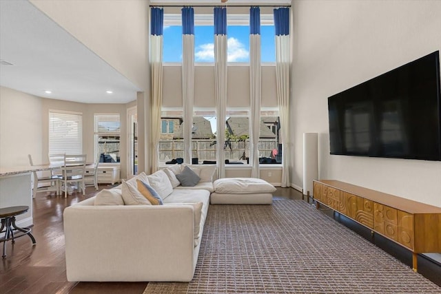 living room featuring a towering ceiling, dark wood-type flooring, and a wealth of natural light