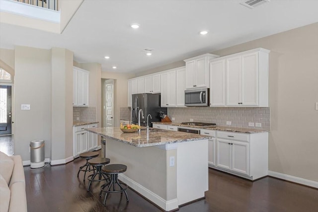 kitchen with white cabinets, stainless steel appliances, an island with sink, and a kitchen bar