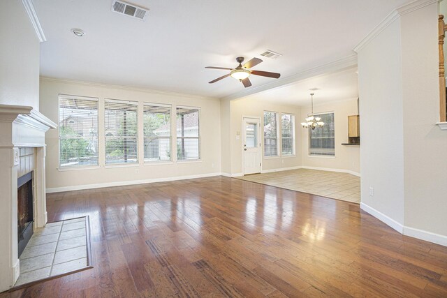 unfurnished living room with ornamental molding, ceiling fan with notable chandelier, a wealth of natural light, and a fireplace