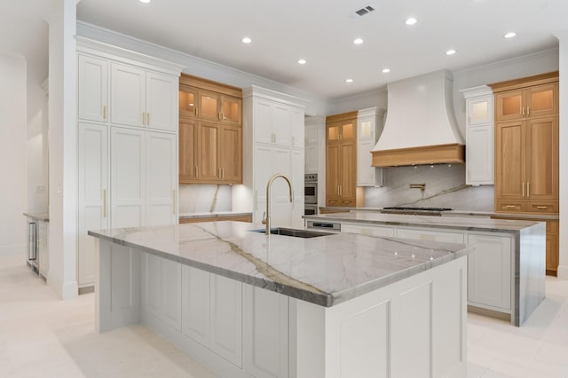 kitchen with sink, custom exhaust hood, a large island with sink, and white cabinets