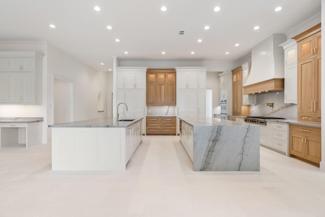 kitchen with light stone counters, custom range hood, a large island, backsplash, and sink