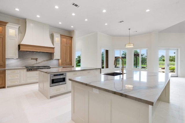 kitchen featuring light stone countertops, premium range hood, decorative light fixtures, a large island with sink, and sink