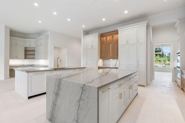 kitchen with sink, a large island, white cabinets, light stone counters, and ornamental molding