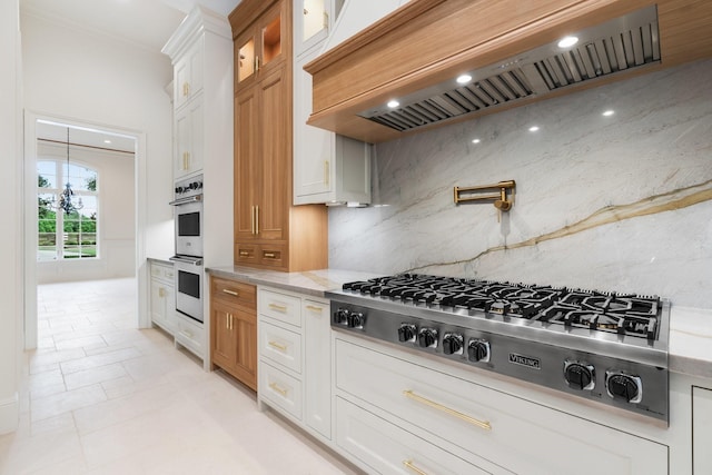 kitchen featuring light stone counters, stainless steel appliances, custom range hood, and white cabinetry