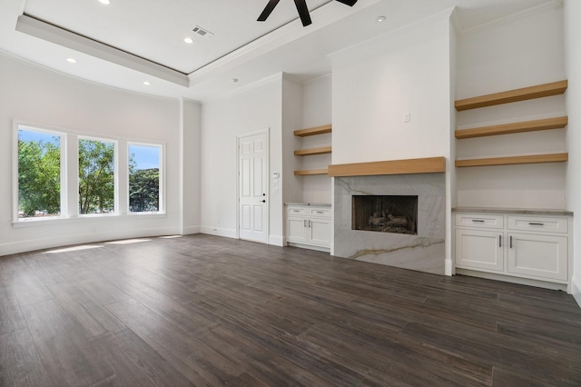 unfurnished living room with dark hardwood / wood-style floors, a premium fireplace, a raised ceiling, ceiling fan, and ornamental molding