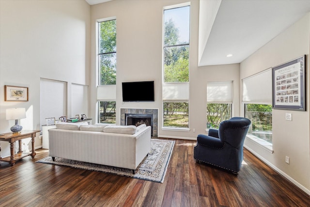 living room with a high ceiling, dark wood-type flooring, and a tile fireplace