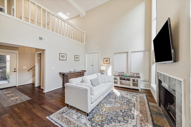 living room with a towering ceiling, dark hardwood / wood-style flooring, a tiled fireplace, and beamed ceiling