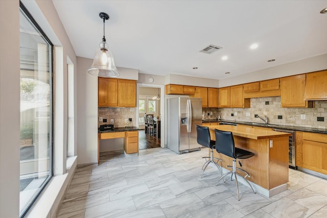 kitchen with pendant lighting, butcher block counters, stainless steel fridge with ice dispenser, a kitchen island, and sink